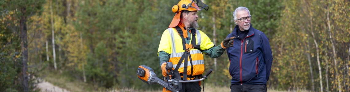Medelålders kvinna i mössa och fleecejacka tittar på sin mobiltelefon i skogen.